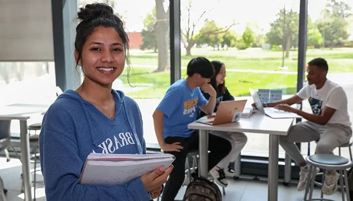 a student poses for a photo with more students at a table behind her